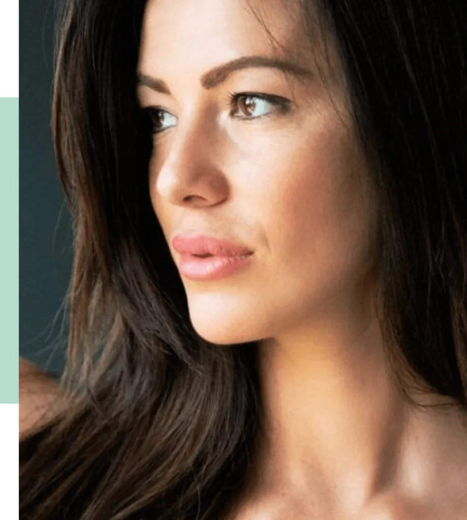 Close-up portrait of a young woman with long dark hair and natural makeup, gazing thoughtfully to the side. The image highlights her facial features, including her smooth skin and defined cheekbones, against a softly blurred background. Ideal for beauty, fashion, or lifestyle content.