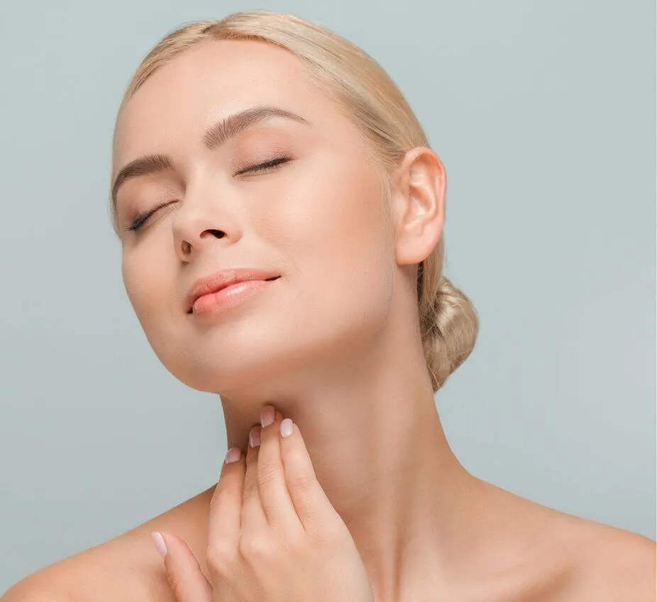 Close-up of a woman with blonde hair and a serene expression, gently touching her neck. She has a natural makeup look, showcasing healthy, glowing skin. The background is a soft, light color, emphasizing her features. This image represents beauty, self-care, and skincare routines. Ideal for articles on skincare tips, beauty products, or wellness practices.