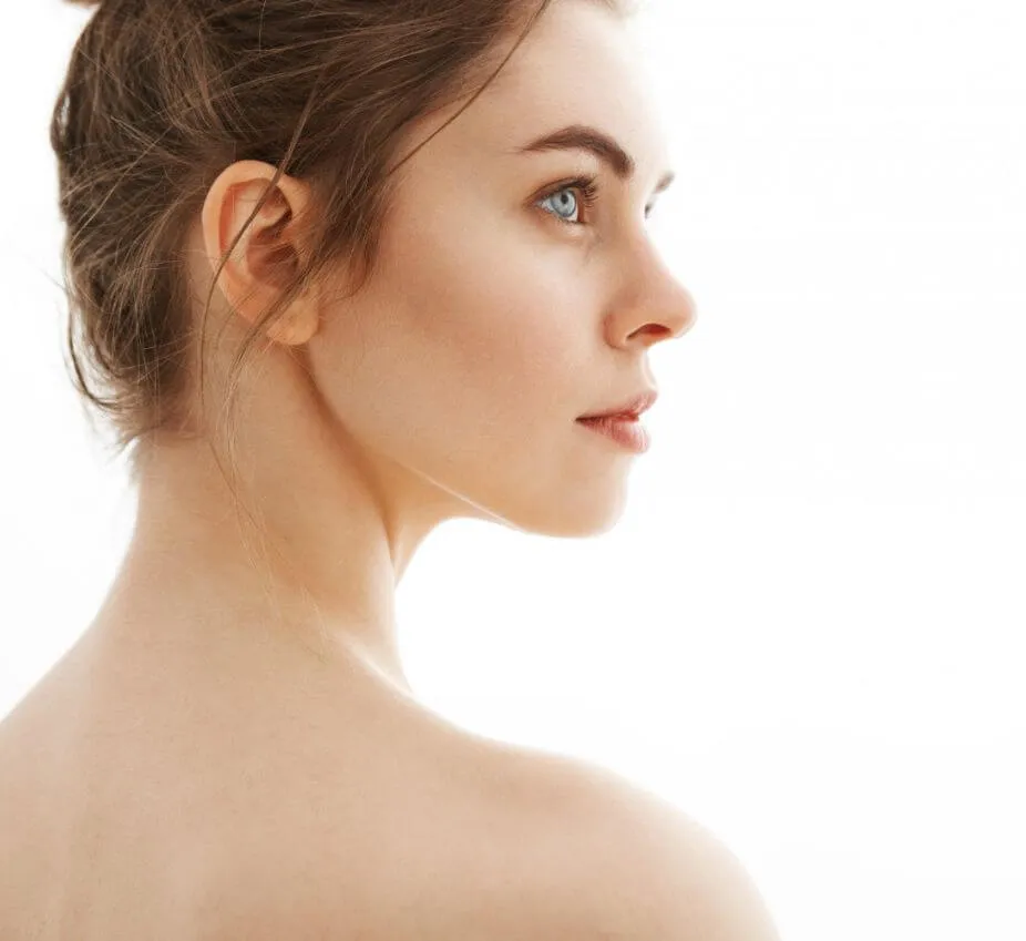 Profile view of a young woman with light skin and blue eyes, showcasing her natural beauty. She has a bun hairstyle, and her expression is calm and contemplative. The background is bright and minimalistic, emphasizing her features. This image can be used to represent themes of beauty, skincare, or wellness in lifestyle content.