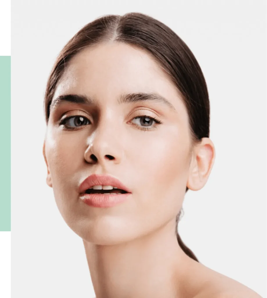 Close-up portrait of a woman with smooth skin and natural makeup. She has straight brown hair, subtle eye makeup highlighting her blue-gray eyes, and a soft pink lip color. The background is minimalistic with a white backdrop, emphasizing her features. This image represents beauty and skincare, making it ideal for topics related to cosmetics, personal care, and fashion. The clean aesthetic and focus on the model's face convey a sense of freshness and elegance, appealing to audiences interested in beauty trends and wellness.