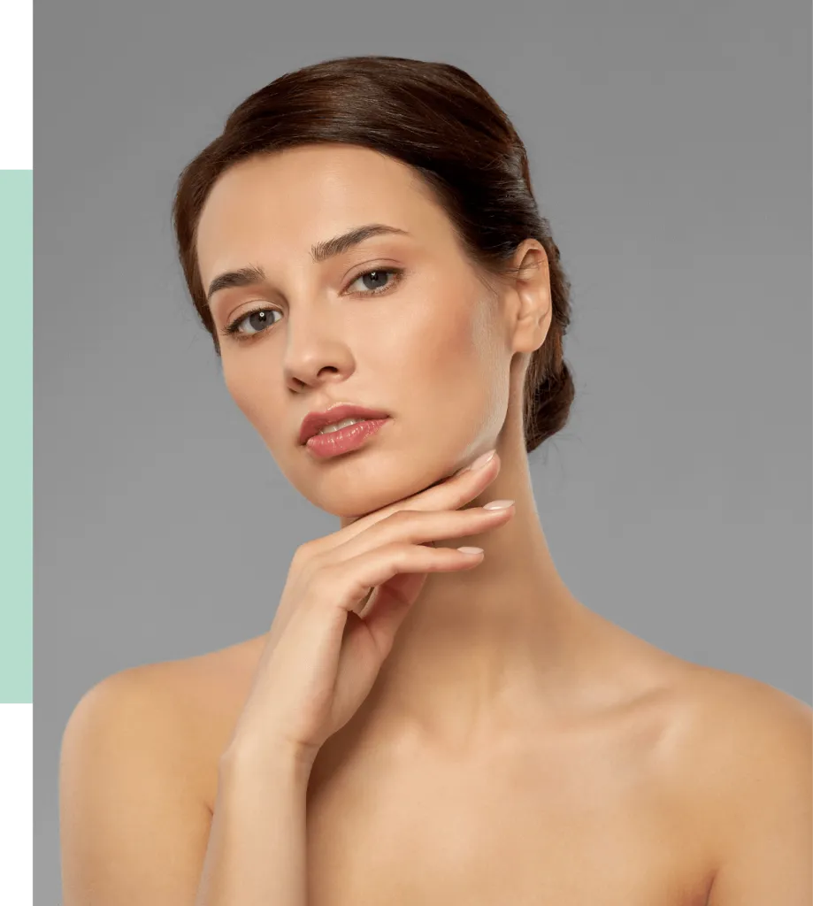 Portrait of a woman with a smooth complexion and subtle makeup, showcasing her natural beauty. She has her hair styled in an elegant updo and is gently resting her chin on her hand, exuding confidence and grace. The background is a neutral gray, enhancing her features. This image highlights skincare and beauty aesthetics, making it ideal for beauty and wellness content.