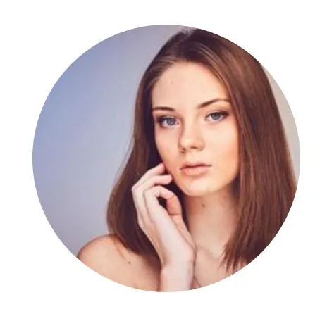 Portrait of a young woman with long, straight brown hair and natural makeup, lightly touching her face with her right hand. The image is framed in a circular crop, highlighting her facial features and soft expression against a gradient background. This photo can be used for beauty, fashion, or lifestyle content.