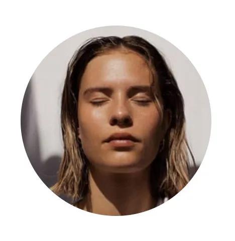 Close-up portrait of a woman with shoulder-length hair, eyes closed, and a serene expression, set against a soft, neutral background. The circular crop emphasizes her relaxed demeanor and natural beauty, showcasing her glowing skin. This image conveys a sense of calm and tranquility, making it suitable for wellness or beauty-related content.