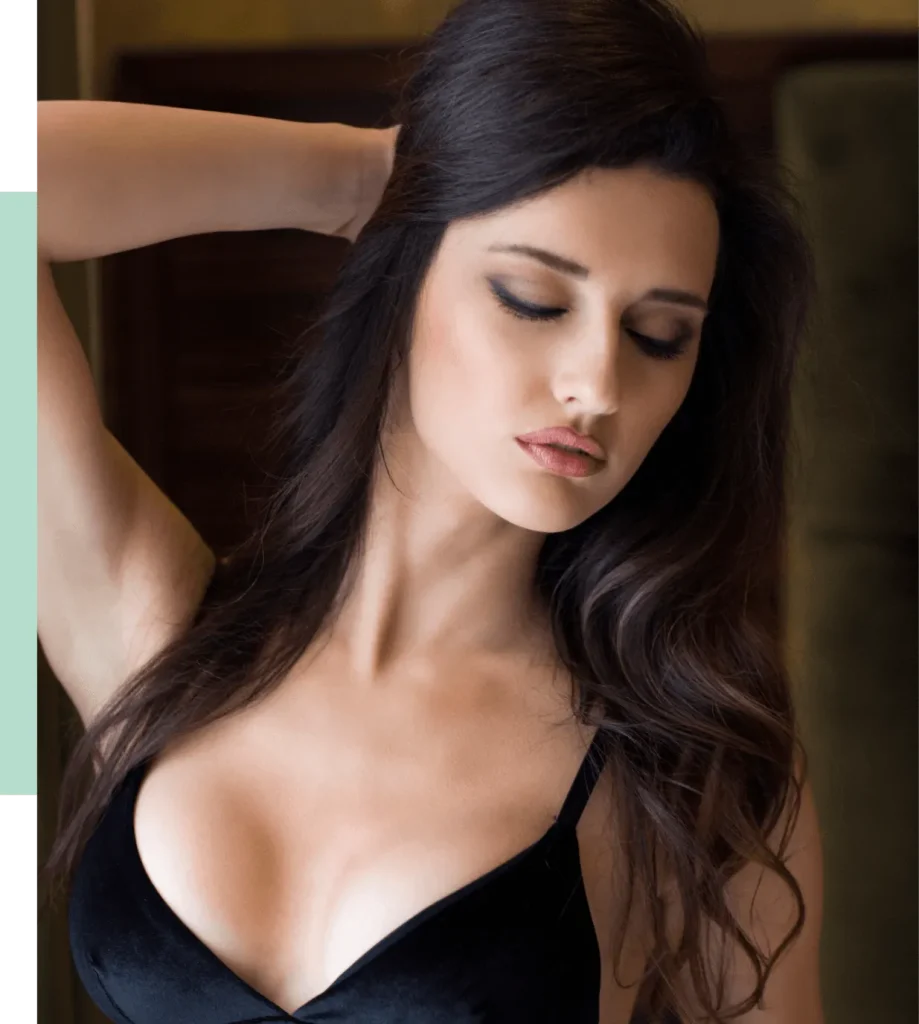 A woman with long, dark hair poses gracefully with her eyes closed, showcasing a black velvet bralette. The soft lighting highlights her facial features and the elegant contours of her neck and shoulders. The background is softly blurred, creating a serene atmosphere that emphasizes her calm expression. This image conveys beauty and confidence, making it suitable for fashion or lifestyle content.