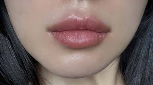 Close-up image of a person's lips showcasing a natural, soft pink lip color with a glossy finish. The lips appear well-hydrated and smooth, highlighting a subtle makeup look. The background is neutral, allowing the focus to remain on the lips. This image can be used to illustrate beauty trends, lip care products, or makeup techniques for a fresh, everyday look.