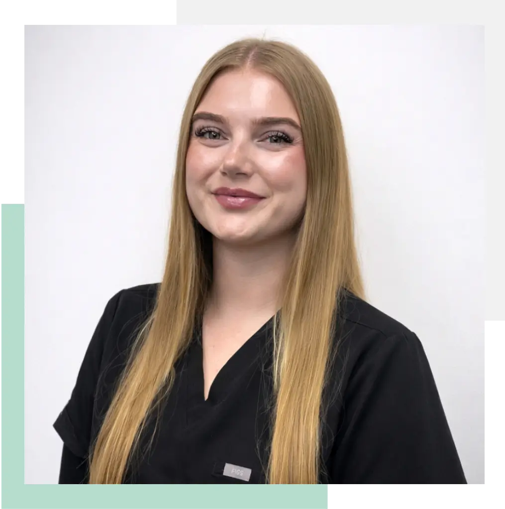 A smiling young woman with long blonde hair is wearing a black medical scrub top. She is posed against a neutral background, exuding a professional and approachable demeanor. The image highlights her friendly expression, making it suitable for a healthcare or medical-related context.